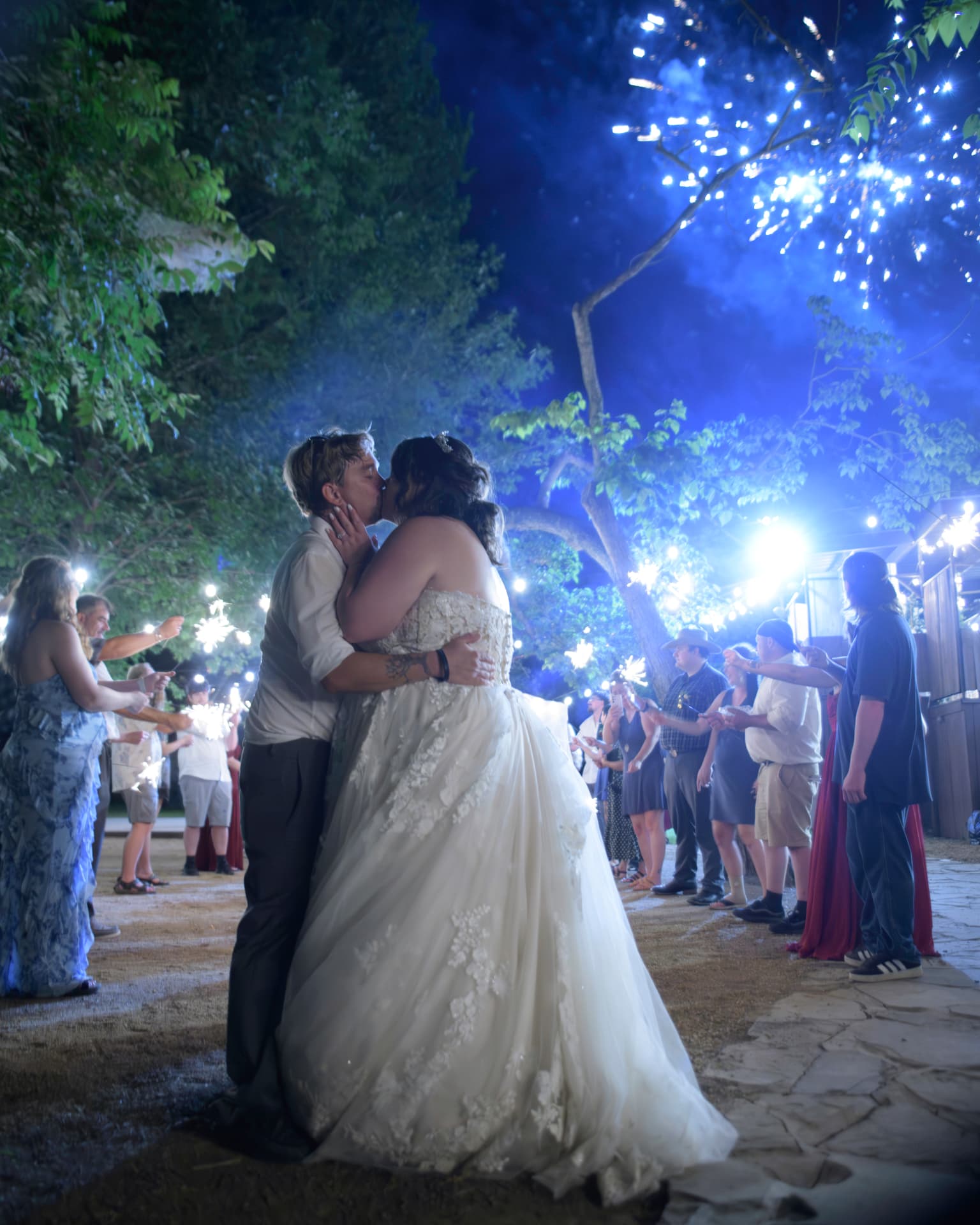 Bride and groom kissing beneath sparklers and string lights during a nighttime send-off