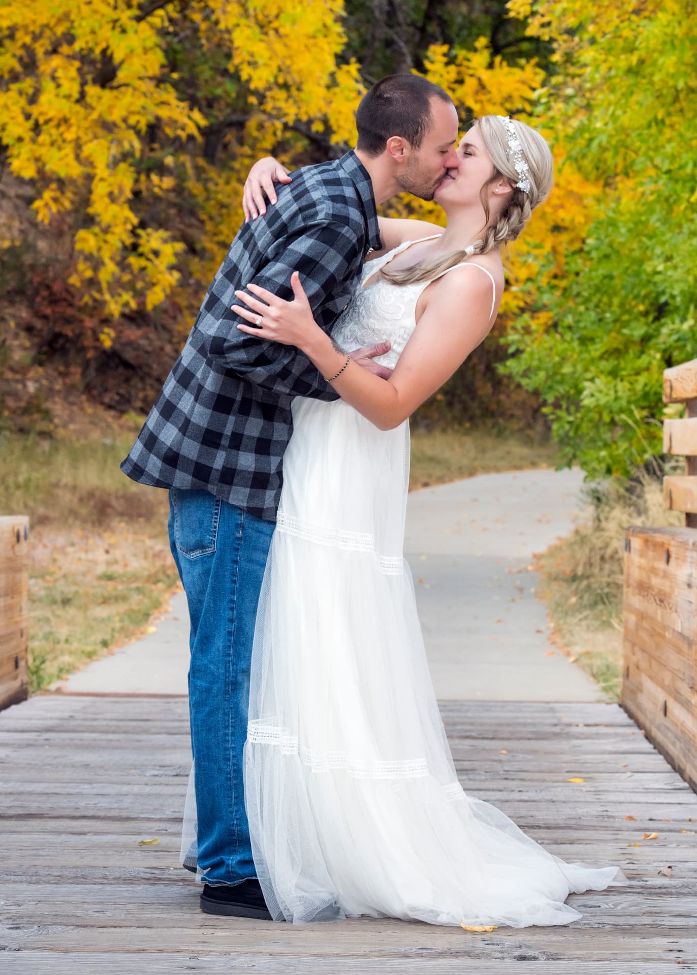 Bride and groom kissing on a wooden footbridge framed by golden autumn trees