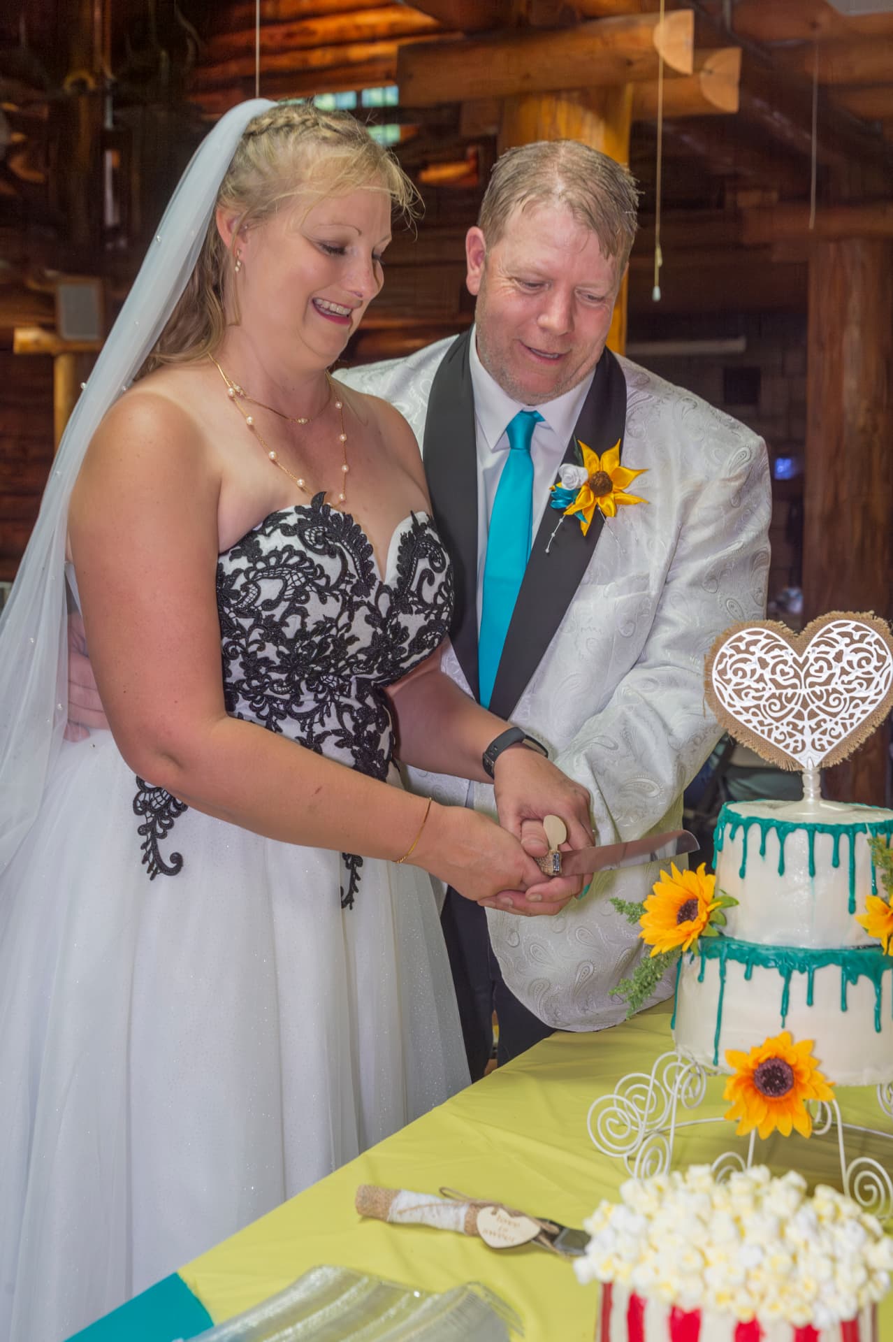 Bride and groom smiling while cutting a sunflower-topped wedding cake together indoors