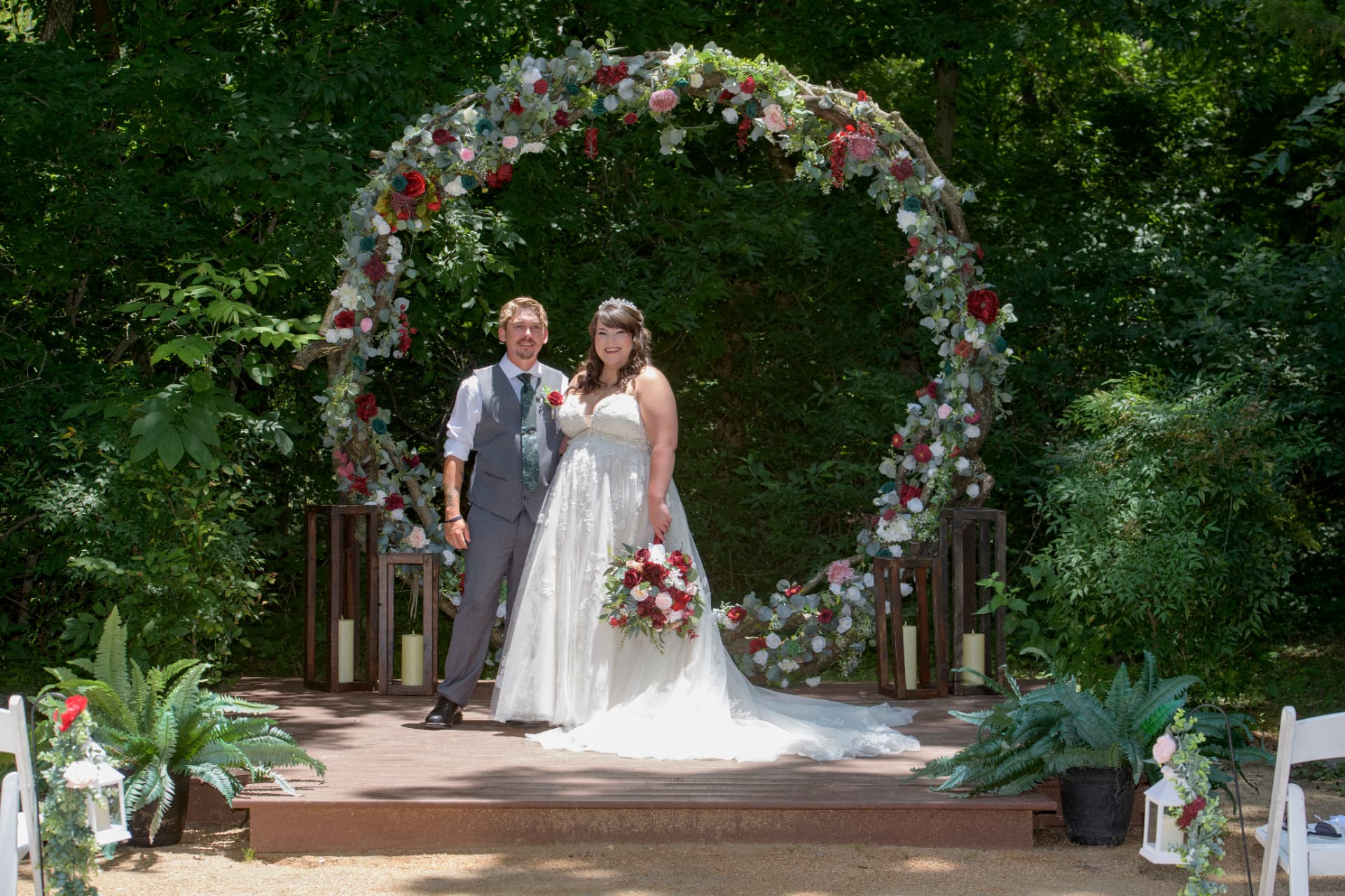Bride and groom standing together beneath a floral-covered wooden arch during an outdoor summer ceremony